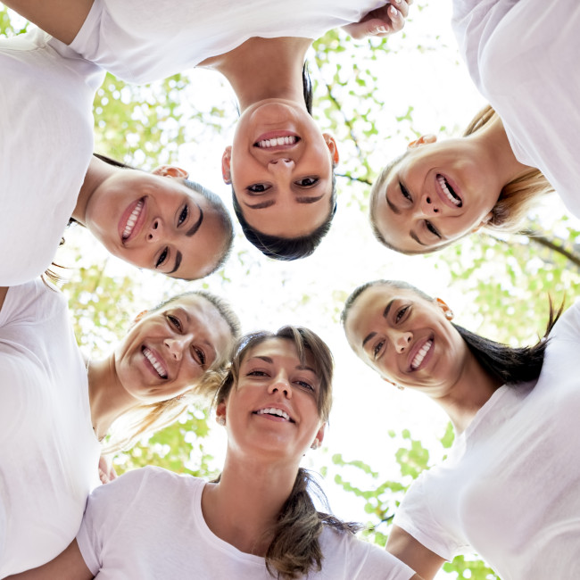 Group of women standing in the circle, smiling at the camera, low angle view.